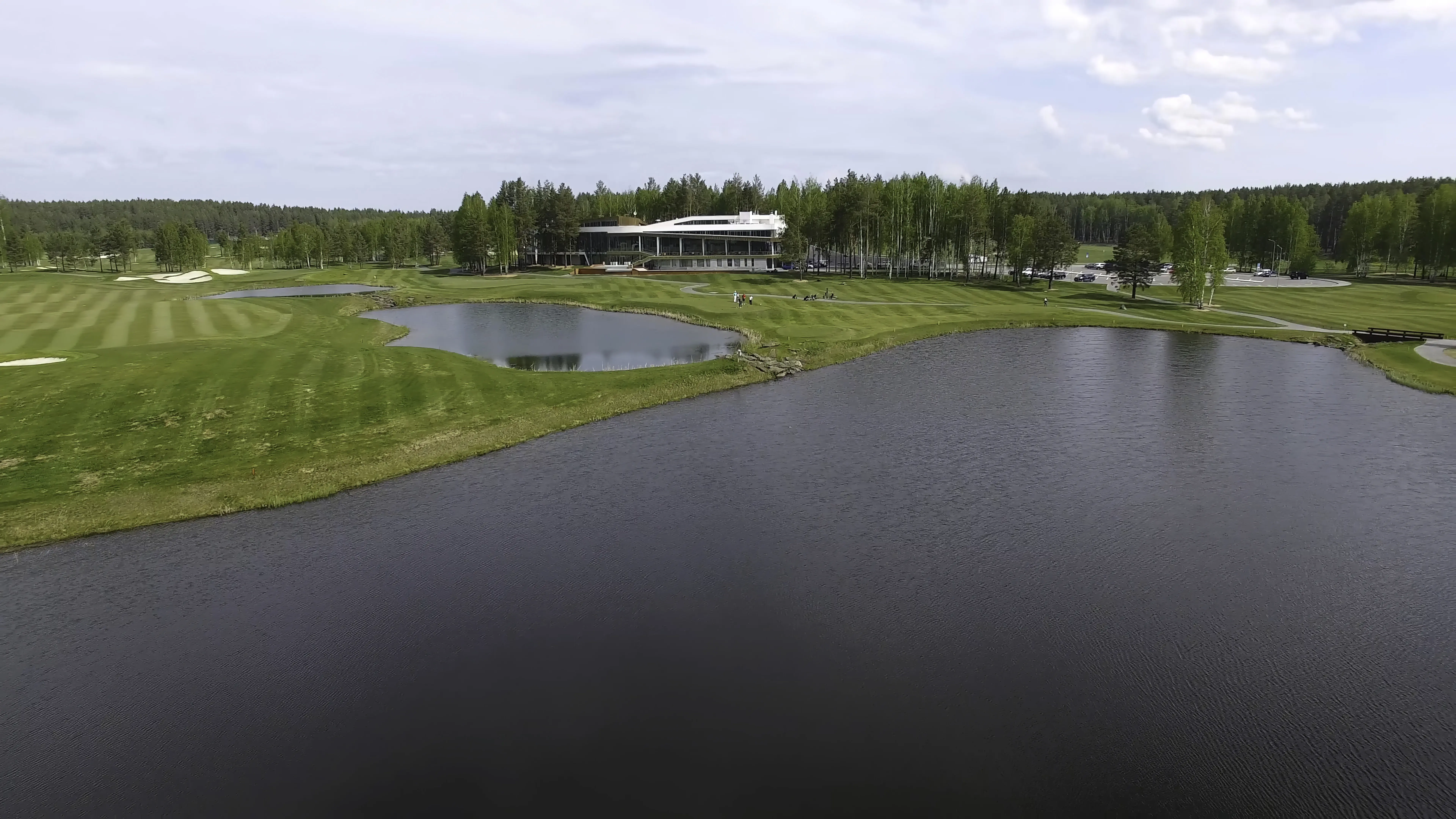 Aerial view of a solar-powered golf cart with clouds in a blue sky at a forest lake golf club.